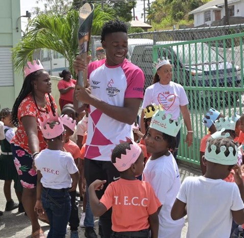 National athlete, Darren Morgan, with Baton in hand, amongst students at one of the schools visited during the Queen’s Baton Relay.