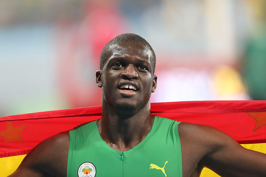 Grenadian 400m runner Kirani James smiling with the national flag draped behind his shoulders after a track event.